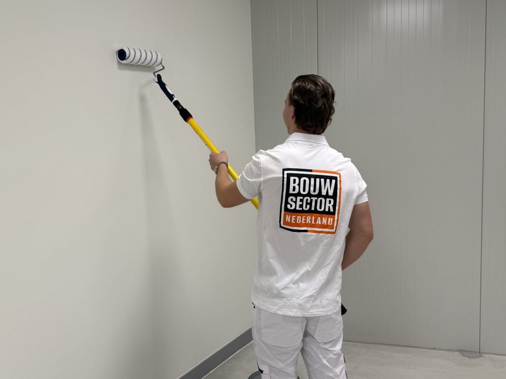 Schilder van Bouwsector Nederland saust een witte wand met een roller op een gele steel