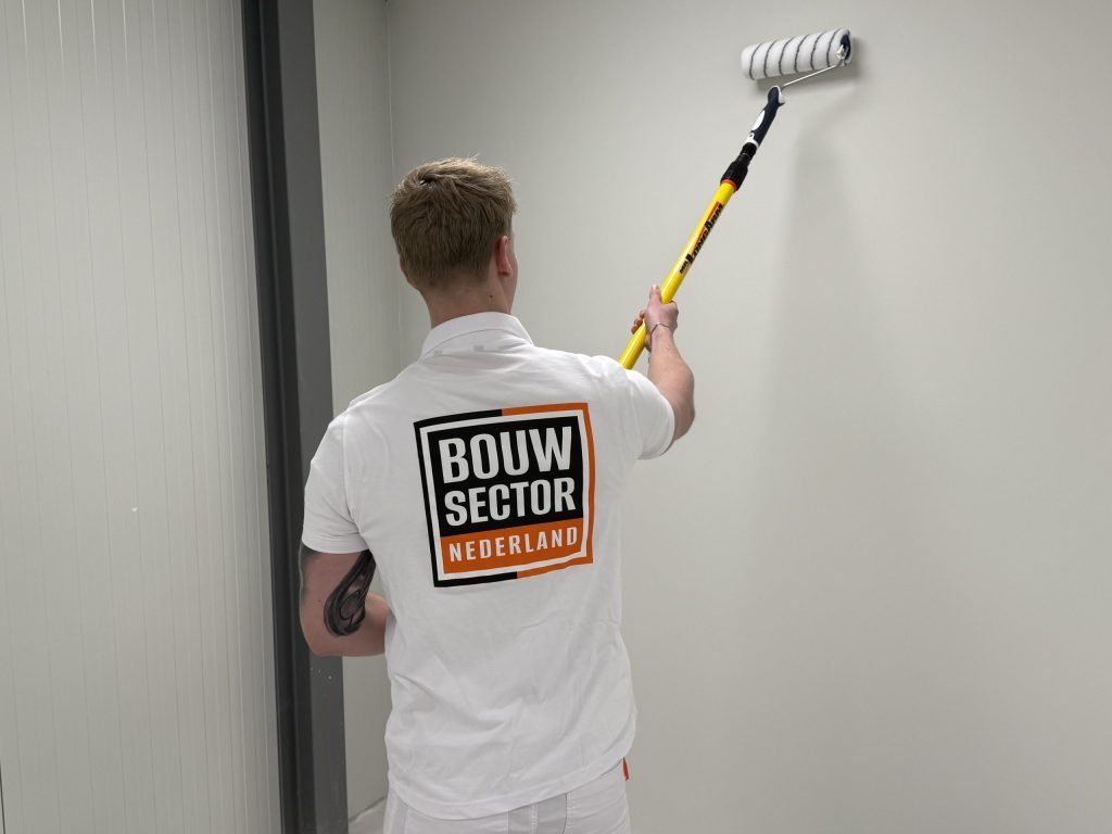 Schilder van Bouwsector Nederland saust een lichte wand in een smalle gang met de roller op een steel