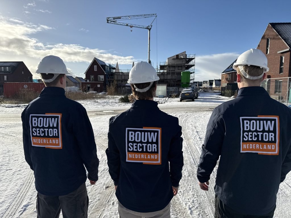 Drie vakmensen van Bouwsector Nederland met witte helm en donkerblauwe jas bij een besneeuwde bouwplaats